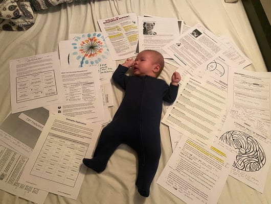 A baby on the bed with various papers around him.